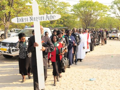 Kuvassa kulkue Namibian luterilaisen kirkon lähtisen hiippakunnan lähetysjuhlilta 2019. Kulkueen kärjessä kyltti, jossa teksti: Indeni nuuyuni auhe, joka tarkoittaa menkää kaikkeen maailmaan.