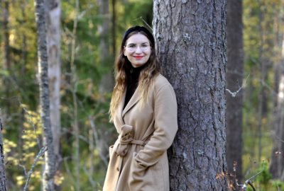 Hanna Ylikangas nojaa metsässä puun runkoon.