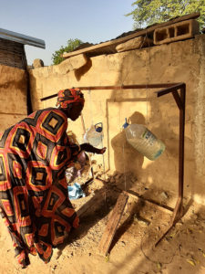 Nainen pesee käsiään pesupisteellä Senegalissa. Vesi valutetaan muoviastioista. 
