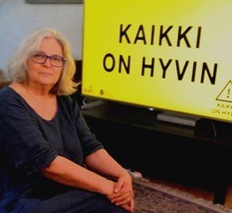 Annukka Häkämies ja TV-ruutu, jossa Evankeliumijuhlien tunnus Kaikki on hyvin.