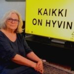 Tamperelainen Annukka Häkämies ja kyltti, jossa on Evankeliumijuhlien tämän vuoden teema "Kaikki on hyvin".