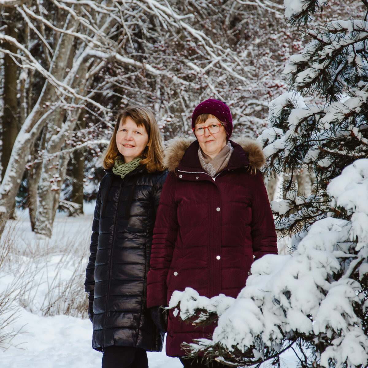 Kaksi naista seisoo lumisessa metsässä.