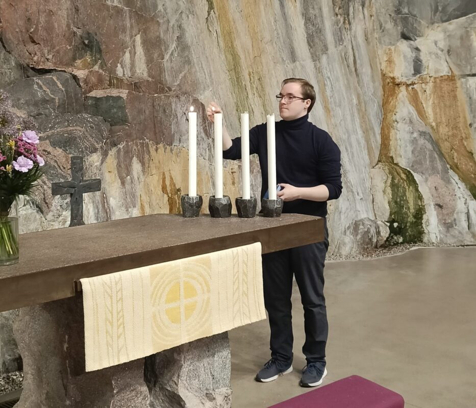 Nuori mies sytyttää kynttilöitä kirkossa.