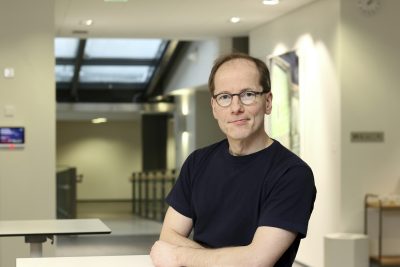 Tutkimusprofessori Timo Partonen seisoo työpaikallaan kädet puuskassa päällään musta t-paita.