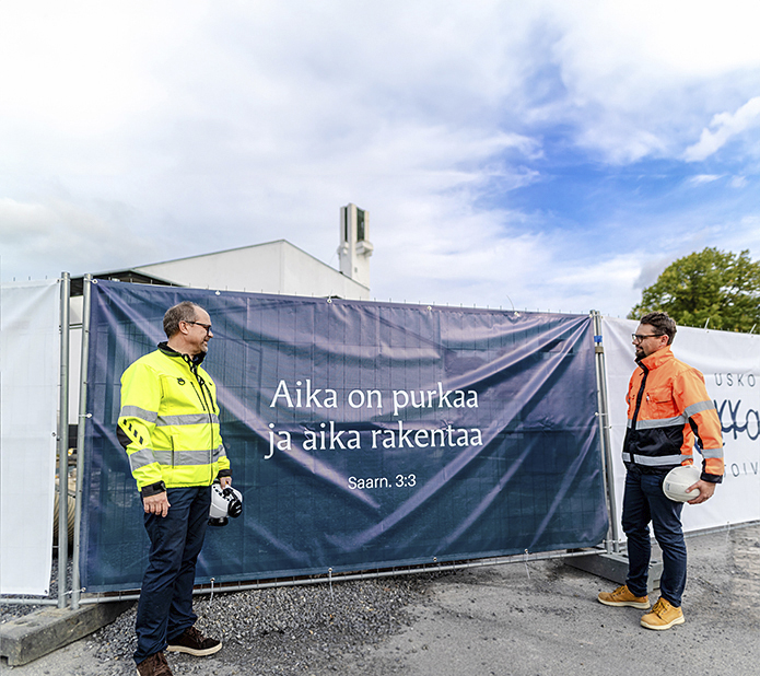 Kaksi henkilöä työmaan aitalakanoiden edessä.