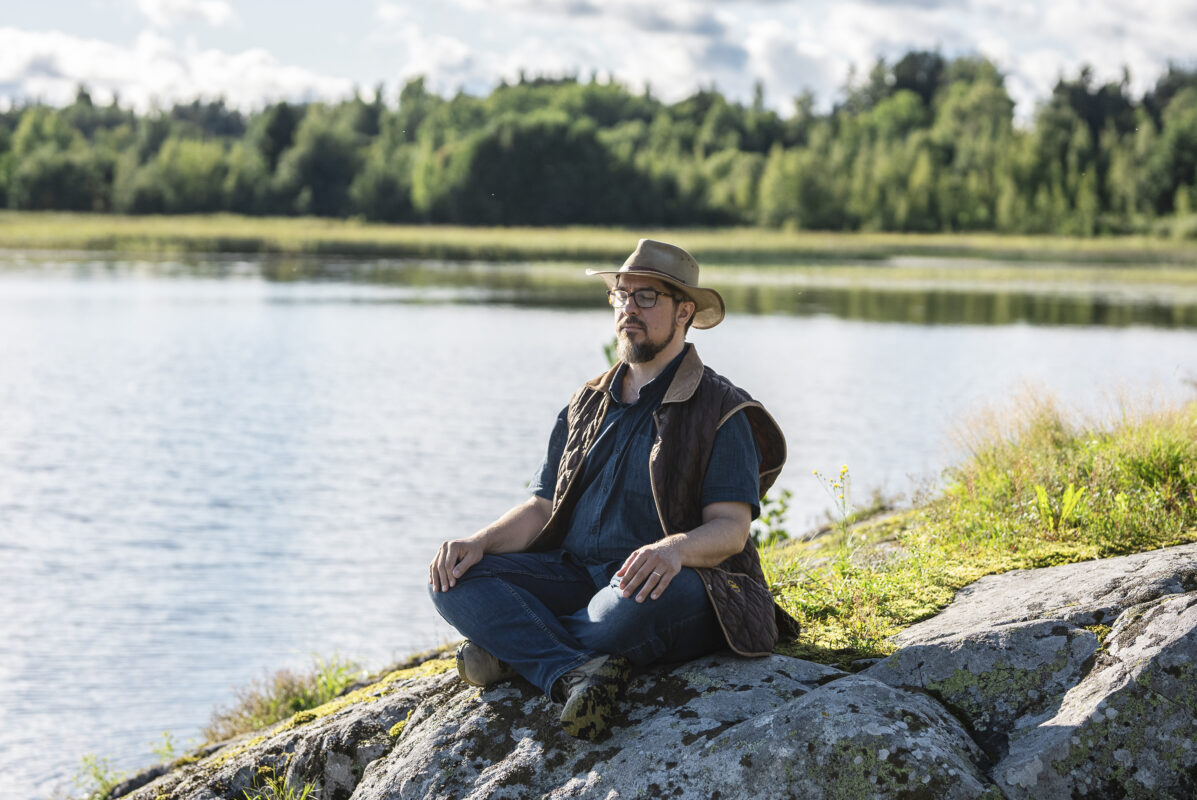 Mika K. T. Pajunen istuu meditoimassa risti-istunnossa rannalla. Silmät ovat kiinni.