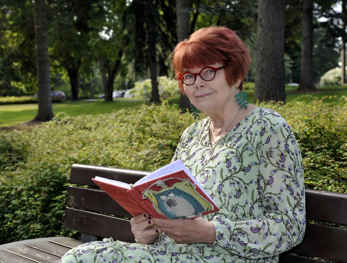 Anne Margit Perttola istuu puiston penkillä ja pitää kädessään päiväkirjaa.