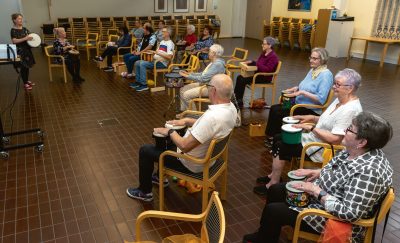Seurakuntakeskuksen salissa joukko senioreita istuu tuoleilla soittimet sylissä ja seuraavat edessä seisovia muskarin vetäjiä Marianne Pellistä ja Ulla Rostén-Lahtea.