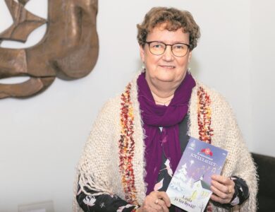 Hymyilevä nainen pitelee käsissään Kauneimpien Joululaulujen lauluvihkoa.