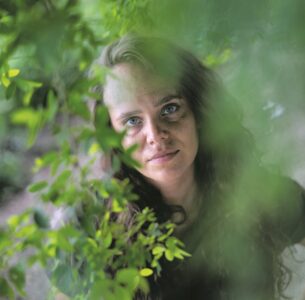 Nainen katsoo lehvästön takaa.