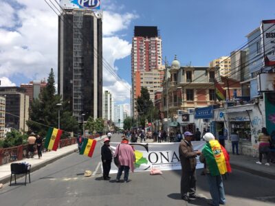 Katunäkymä, jossa taustalla suuria pilvenpiirtäjiä, etualalla ihmiset aloittamassa mielenosoitusta banderollein.