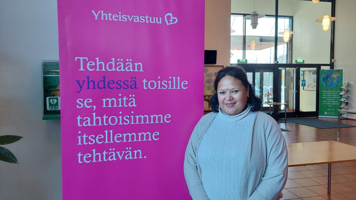 Nainen seisomassa rollupin edessä, jossa lukee Yhteisvastuu - Tehdään yhdessä toisille se, mitä tahtoisimme itsellemme tehtävän.