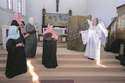 Neljä hunnutettua ihmistä kirkon alttarilla ja viides, joka on pukeutunut enkeliksi.