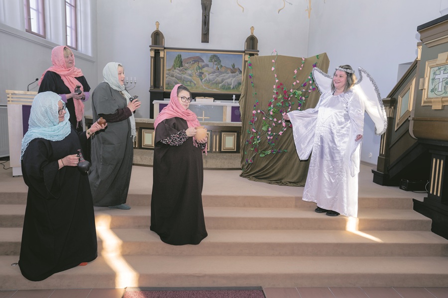 Neljä hunnutettua ihmistä kirkon alttarilla ja viides, joka on pukeutunut enkeliksi.