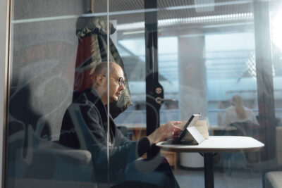 Timo Suutarinen istuu tabletin äärellä kirjaston lasisessa työskentelytilassa.