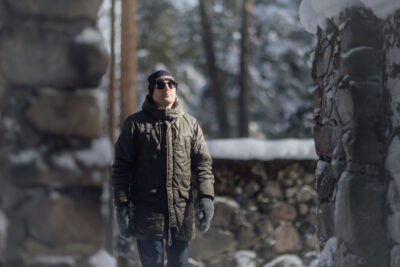 Timo Suutarinen kävelee ulkona. Taustalla kivistä muuria.