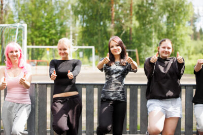 Rippikoululaisia ulkona näyttämässä kuvaajalle peukkuja. Taustalla urheilukenttää.